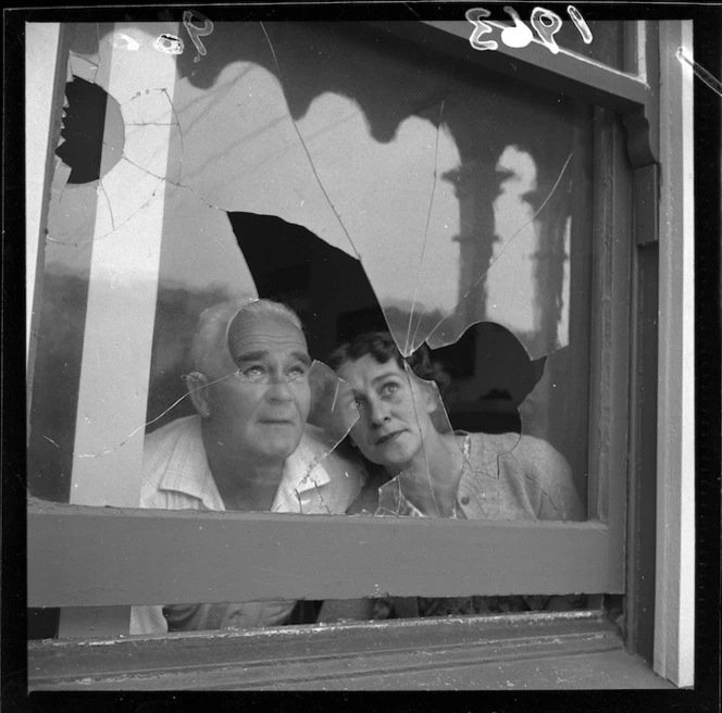 Mr and Mrs Beaty looking through a broken window. Black and white